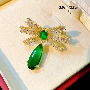 Détail d'une broche nœud dorée avec zircons blancs et pendentif goutte vert