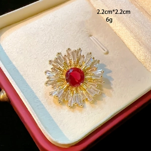 Detailed close-up of a 2.2cm sunburst brooch with red zircon and crystal rays in a box