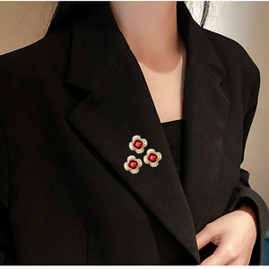 Three gold clover brooches with red stones and white crystals on a black suit lapel