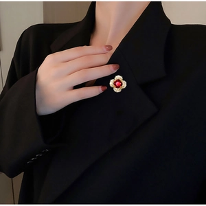 Close-up of a gold flower brooch with red gemstone and diamonds on a black blazer lapel