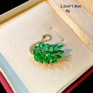 Close-up of golden swan brooch with green crystals and white cubic zirconia details