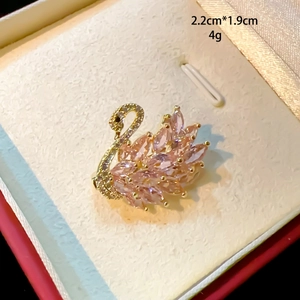 Detailed macro view of an elegant gold swan brooch with pink gemstones and micro-pave crystals
