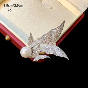 Detailed close-up of a silver butterfly brooch with pavé zircon and a large round pearl