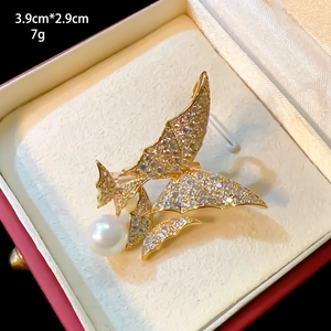 Close-up of elegant butterfly brooch with zircon pavé, gold finish and a white pearl