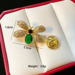 Elegant gold bee brooch with green stone and white zircon wings in a jewelry box