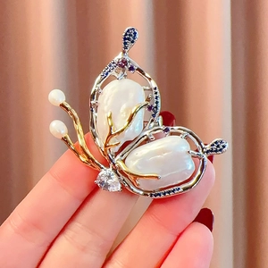 Elegant butterfly brooch with baroque pearls and zircon stones on warm fabric background