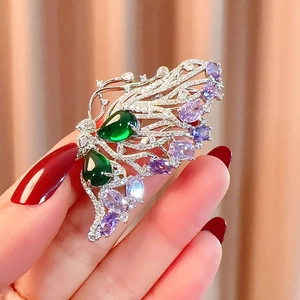 Detailed close-up of butterfly brooch with emerald main stones and purple crystals