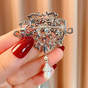 Close-up of vintage silver brooch with zircon pavé and teardrop pearl pendant