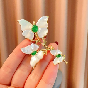 Elegante spilla a farfalla dorata con ali di conchiglia e gemma verde su giacca