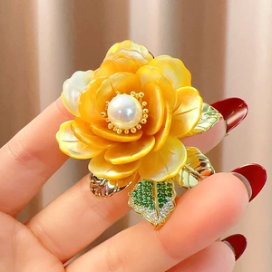 Détail macro d'une broche pivoine en nacre avec perle centrale et feuilles en cristal vert