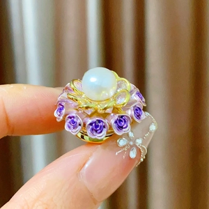Détail d'élégante broche florale avec perle blanche et roses en émail violet sur pétales dorés