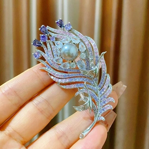 Peacock feather brooch with purple zircon, grey pearl and bird design in hand