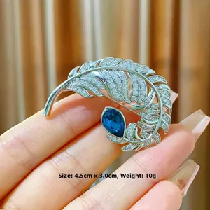 Detailed view of a silver feather brooch with a large blue teardrop gemstone and white zircons
