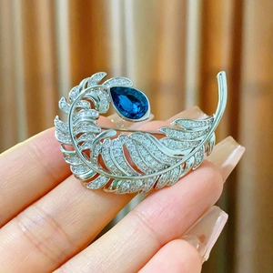 Elegant feather brooch featuring a pear-cut blue stone and white pavé crystals