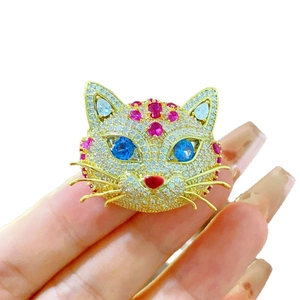 Main tenant une broche chat en or sertie de zircones blancs, bleus et roses