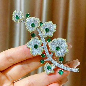 Dettaglio ravvicinato di una spilla floreale argento con pietre verdi e micro-pavé