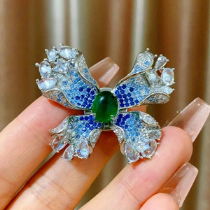 Détail d'une broche papillon argentée avec pierre précieuse verte et cristaux bleus