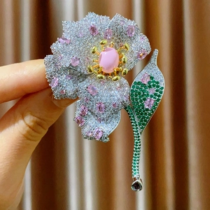 Macro shot of a floral brooch with pink oval stone and micro-pave zircons held by hand