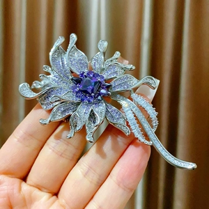 Elegant silver flower brooch with purple zircon held by hand against curtain background