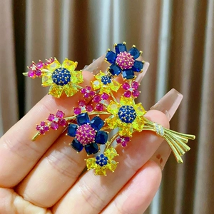 Élégante broche fleur dorée avec cristaux colorés tenue à la main sur fond doux plissé