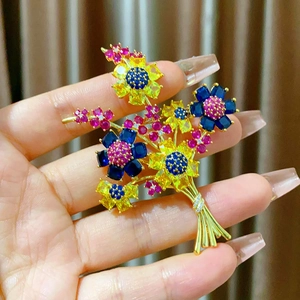Détail d'une broche bouquet de fleurs dorée avec cristaux jaunes et bleus sertis