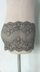 Detail shot of black floral lace fabric with scalloped edges on a female torso model