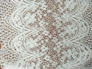 Détail de dentelle blanche ajourée avec motifs floraux et bordure ondulée