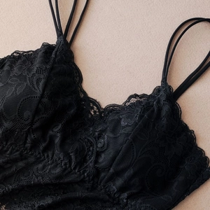 Close-up of black floral lace fabric with triple shoulder straps and scalloped edges