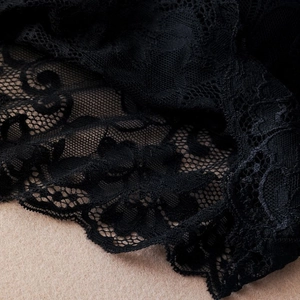 Close-up of black floral lace fabric with scalloped edges and intricate mesh details