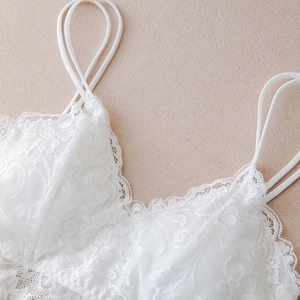 Macro detail of intricate white lace floral texture and slim elastic straps on camisole