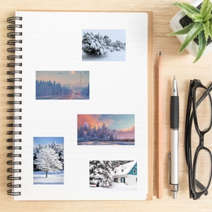 Winter snow scene stickers decorating a spiral notebook on a wooden desk with stationery