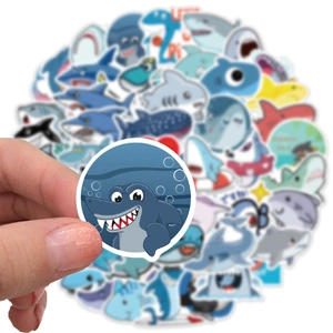 Hand holding a cute cartoon shark sticker from a waterproof decorative set for laptops