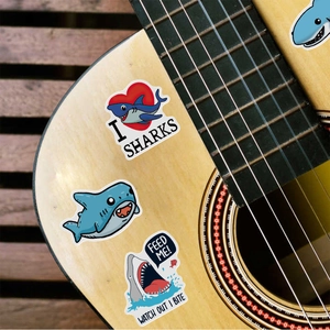 Close-up of cute cartoon shark stickers applied to a wooden guitar surface