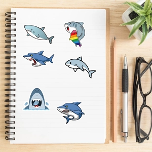 Detail of cute shark stickers on a white notebook with office supplies on a wooden desk