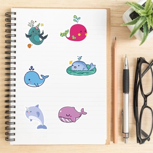 Flat lay of cute cartoon whale stickers on a notebook with stationery and wood background