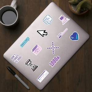 Close-up of retro purple pixel art stickers on a silver laptop with aesthetic desk decor