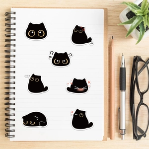 Close-up of cute cartoon black cat stickers with various expressions on a notebook page