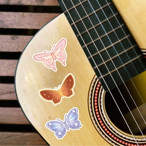 Three colorful butterfly stickers displayed on an acoustic guitar with detailed wing patterns