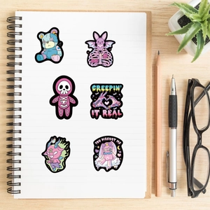 Detailed view of six pastel goth vinyl stickers on a notebook with stationery and a plant