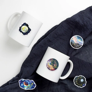 Detailed view of moonlight planet stickers on a white mug and blue textured fabric