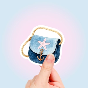 Detail showing a mini denim bag sticker with starfish and anchor charm held by hand
