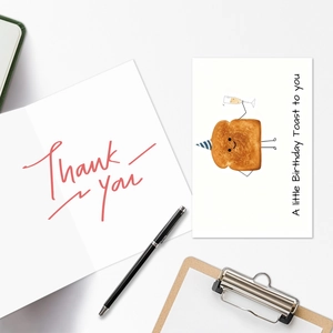 Flat lay of a funny cartoon toast birthday card and a thank you card with white envelope