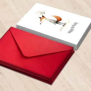 Watercolor fox birthday card set with bright red envelopes on light wood background