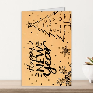 Close-up of a festive Happy New Year folding card with minimal tree icons on a wooden desk