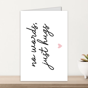 Dettaglio di un biglietto d'auguri bianco con testo No words just hugs su legno