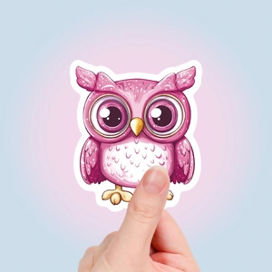 Close-up of a hand holding a cute pink owl sticker with large eyes and white borders