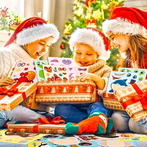 Three happy children wearing Santa hats unboxing DIY sea animal stickers near a Christmas tree
