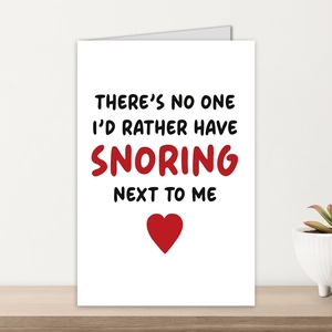 Detail of white matte greeting card with snoring quote and red heart on wood shelf
