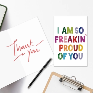 Detalle de tarjetas de felicitación blancas con textos 'Thank You' y 'Proud of You' en escritorio