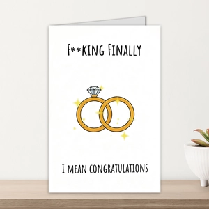 Nahaufnahme einer Hochzeitskarte mit Goldringen und Pflanze auf einem Holzregal